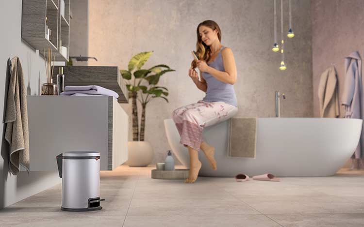 A woman is sitting on a bath tub, a bathroom waste bin is standing at the front 