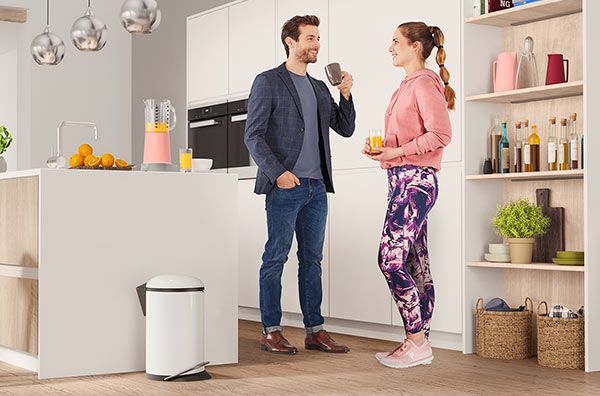 A man and a woman standing in a kitchen next to a waste bin