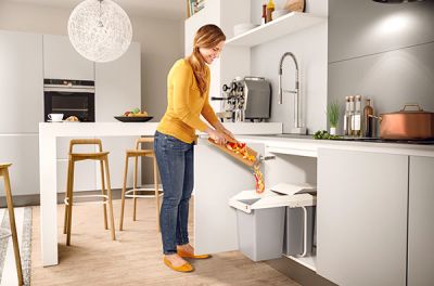 A man and a woman standing in a kitchen next to a waste bin