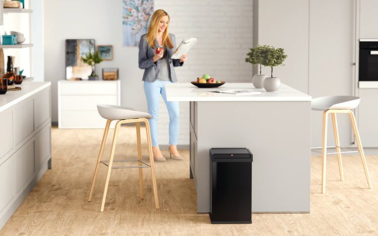 A woman is standing in a kitchen, in the front is a black waste bin