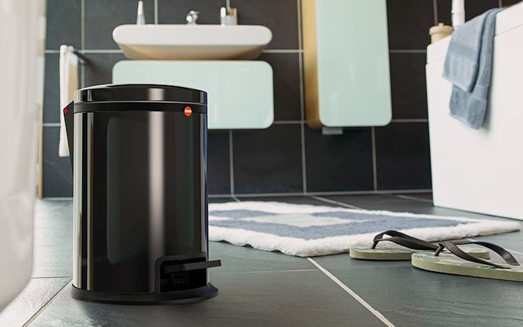 A black waste bin is standing in a bathroom