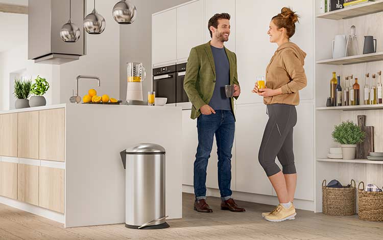 2 people standing in a kitchen next to a waste bin