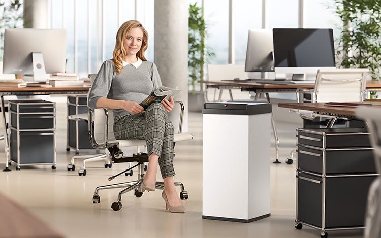 A woman is sitting in an office next to a waste bin