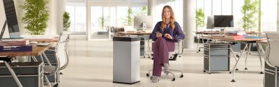 A woman is sitting in an office, next to her is a Hailo Big-Box Swing XL waste bin.