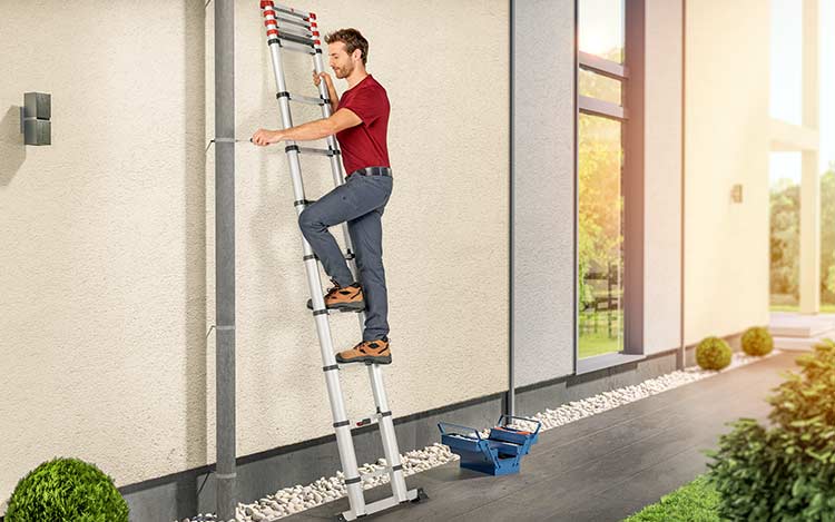 Man standing on a telescopic ladder repairing the downpipe of a gutter