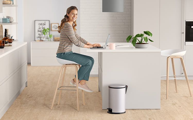 A woman sits in the kitchen at her laptop