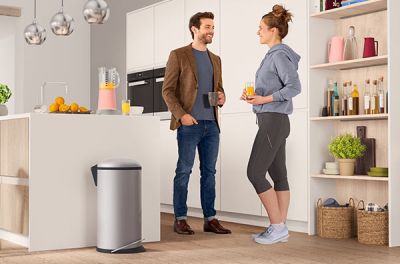 2 people standing in a kitchen next to a waste bin