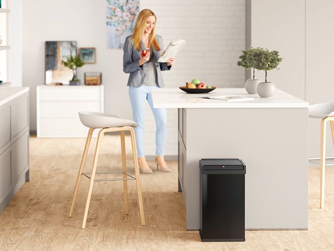 A black sqared waste bin is standing in a kitchen