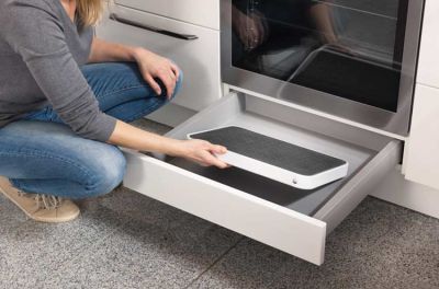 A woman stows a small folding step in a drawer under the stove