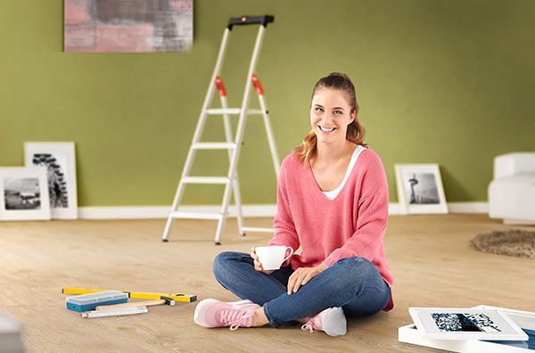 A woman is sitting on the floor of a living room, in the background is a Hailo L60 StandardLineladder